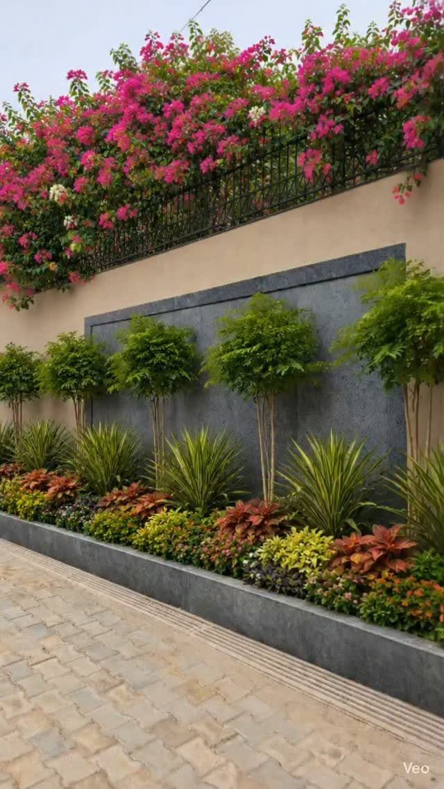 Small green trees and colorful ornamental plants arranged in a modern grey garden bed against a wall.