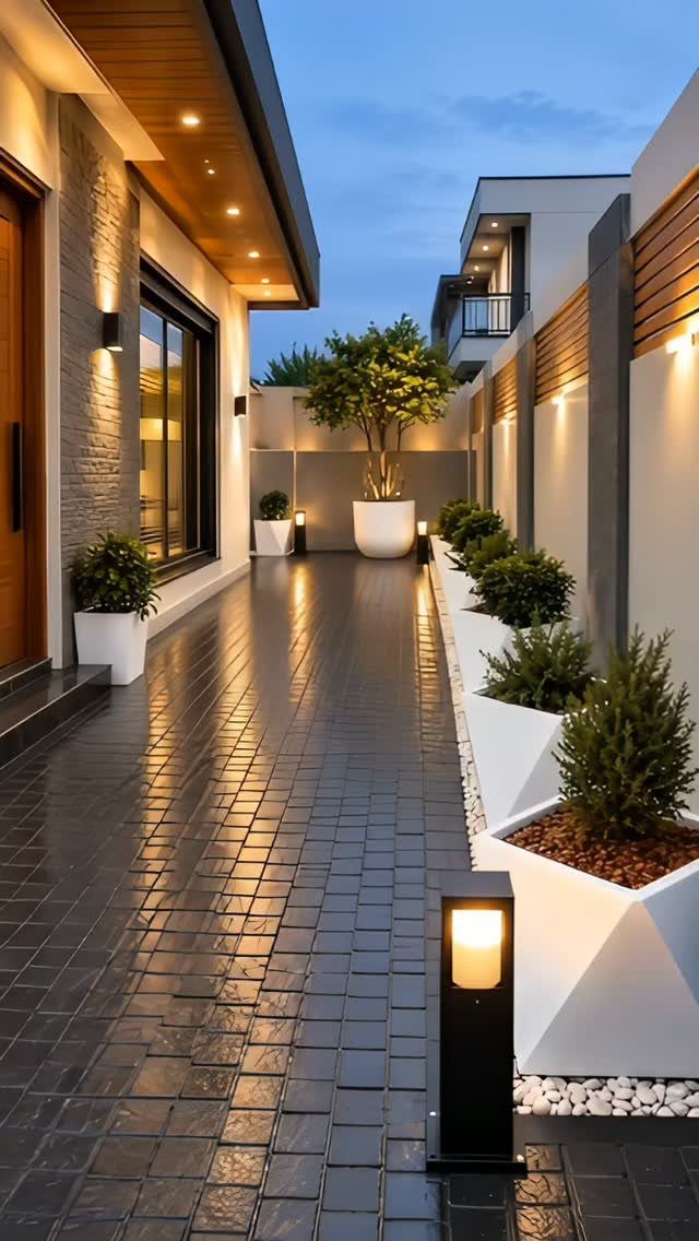 Dark tiled walkway lined with white geometric planters and warm outdoor lighting next to a modern house.