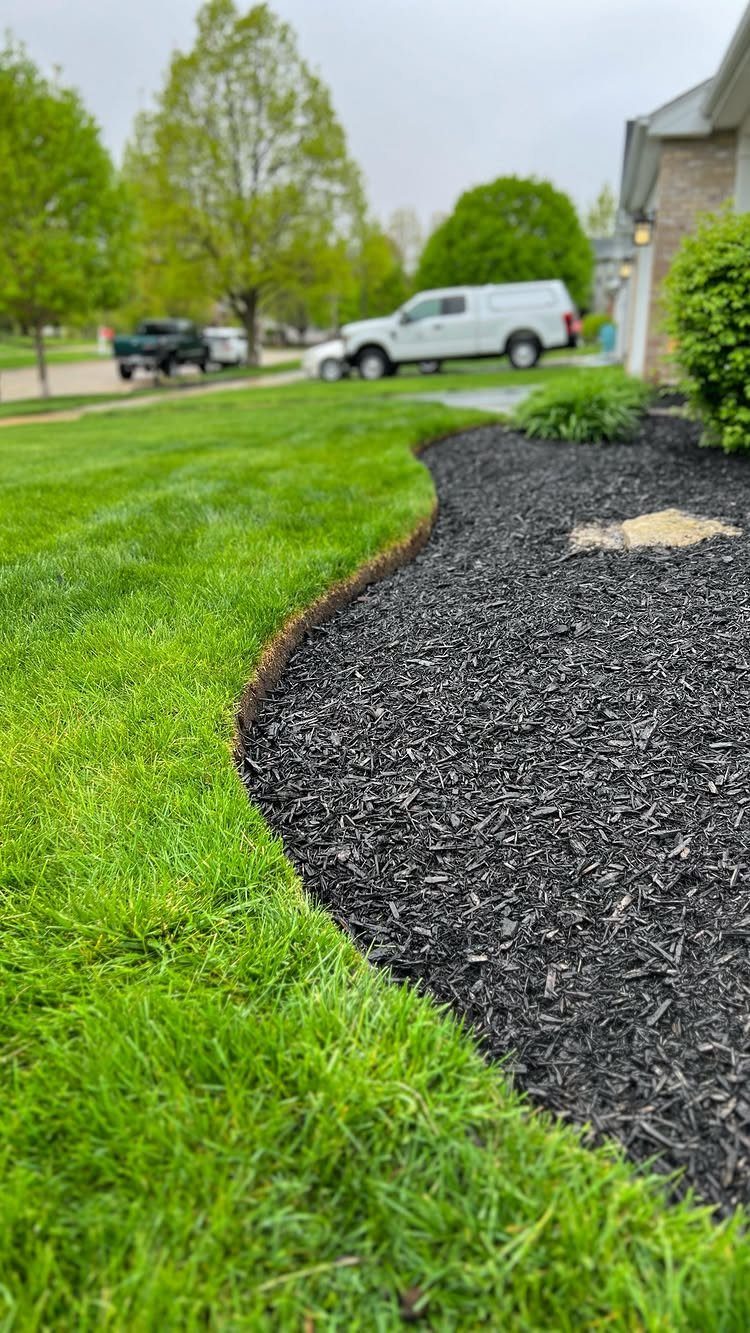 Dark black mulch in a curved garden bed meeting a bright green grass lawn edge.