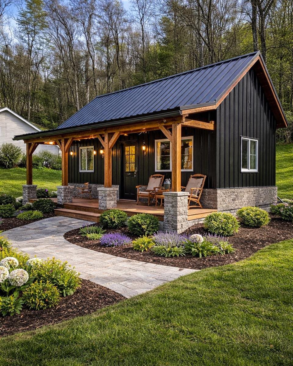 9 Modern Farmhouse Shed Ideas for Your Backyard 3 Black farmhouse shed with a metal roof and wooden porch surrounded by a landscaped garden.