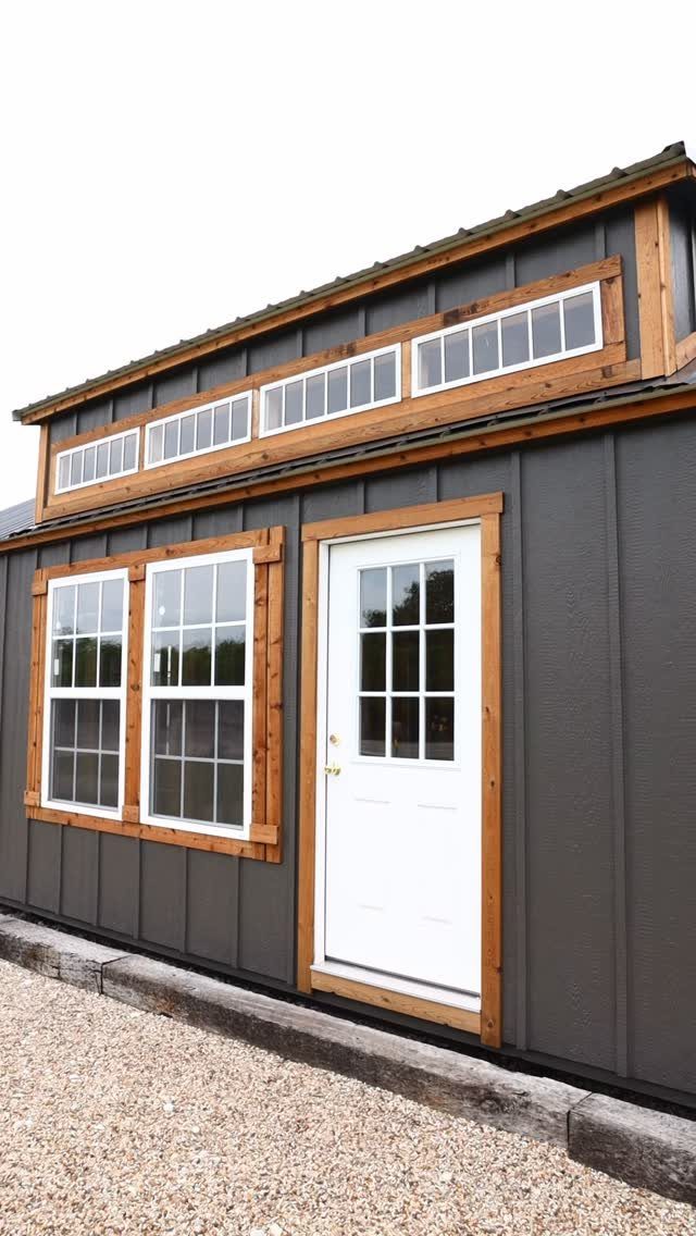 9 Modern Farmhouse Shed Ideas for Your Backyard 8 A modern farmhouse style shed with dark grey siding and light wood trim around the windows and door.