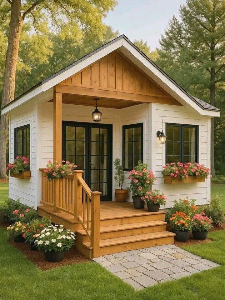 9 Modern Farmhouse Shed Ideas for Your Backyard 7 A white modern farmhouse shed with a wooden porch and colorful flower boxes.