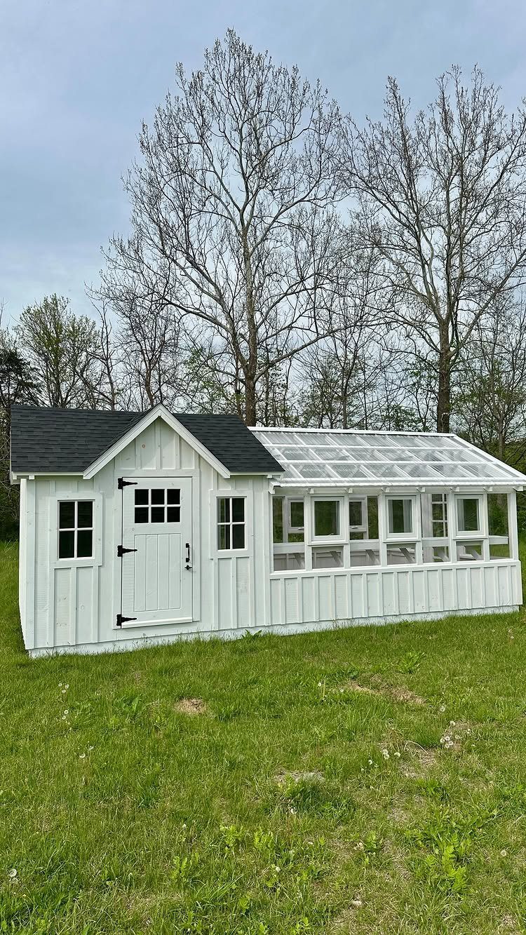9 Modern Farmhouse Shed Ideas for Your Backyard 2 White board and batten shed with an attached glass greenhouse on a grassy field.