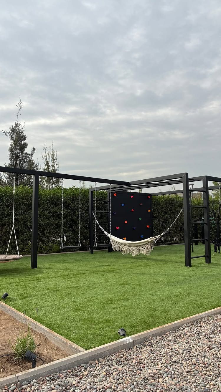22 Outdoor Backyard Ideas for Dining, Gardens, and Gathering Spaces 20 Black metal play structure with a hammock, swings, and a colorful climbing wall on green grass.