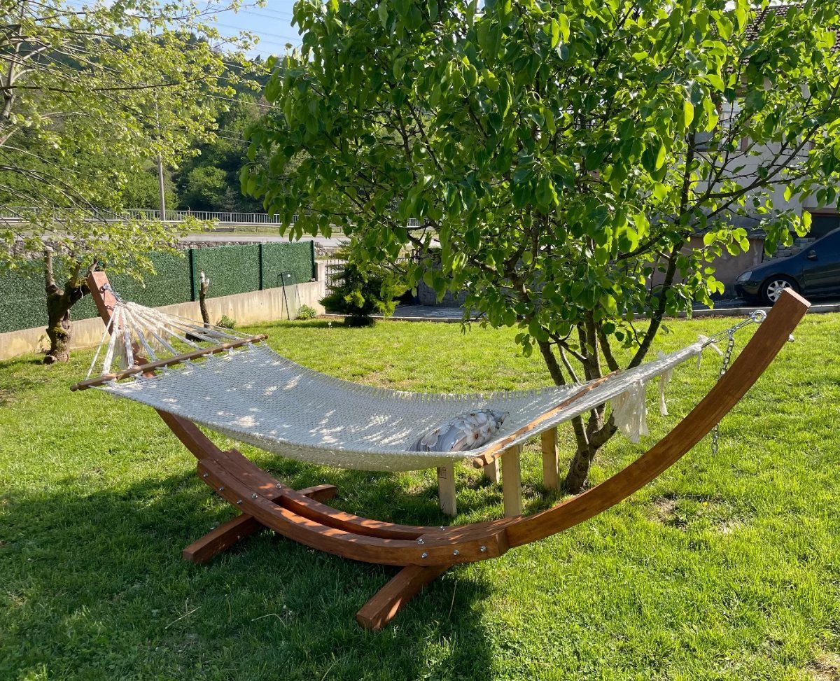 22 Outdoor Backyard Ideas for Dining, Gardens, and Gathering Spaces 18 A white rope hammock on a wooden stand sits on a green lawn next to a tree.