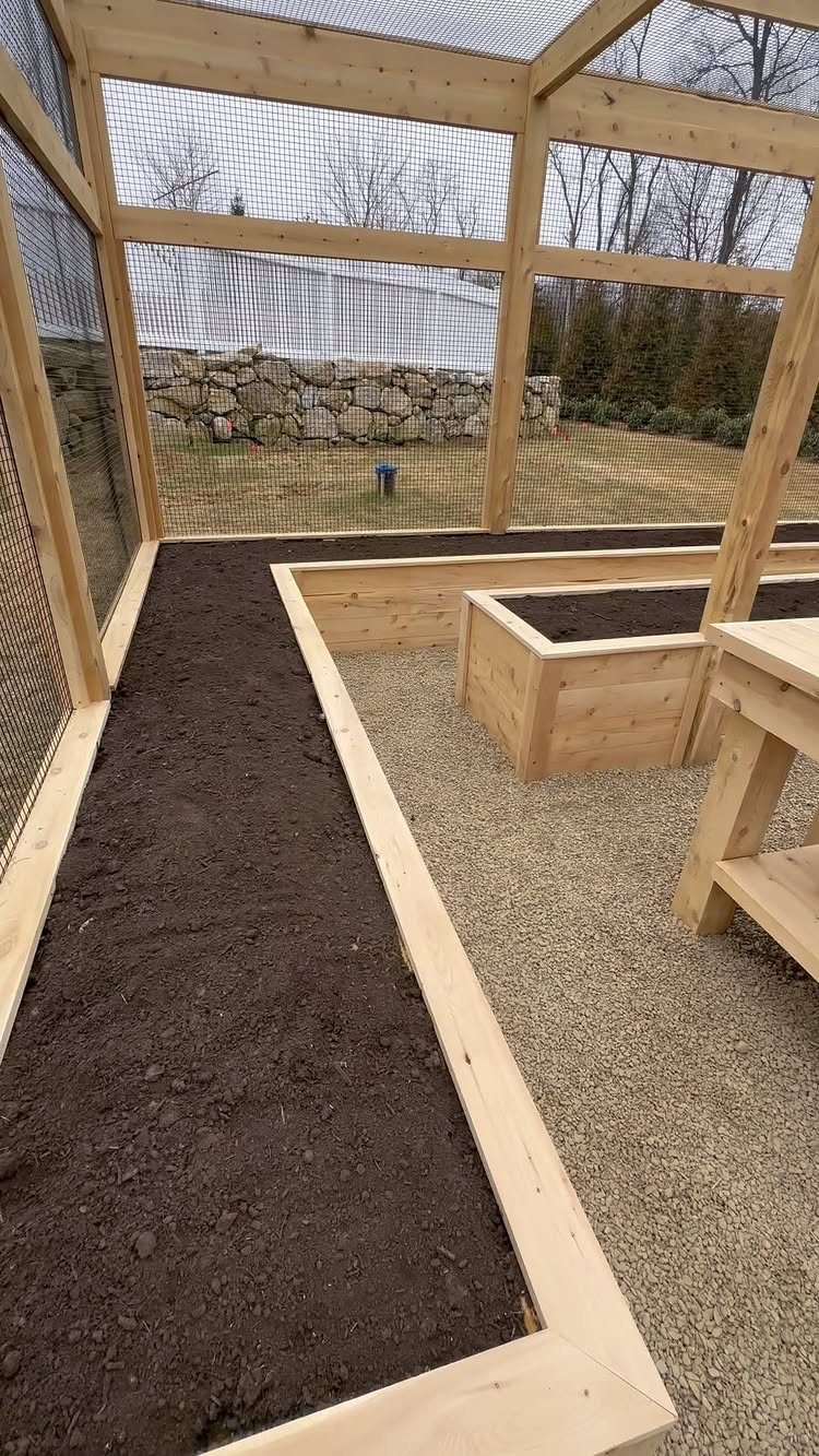22 Outdoor Backyard Ideas for Dining, Gardens, and Gathering Spaces 3 Wooden raised garden beds filled with dark soil inside a large wire mesh enclosure.