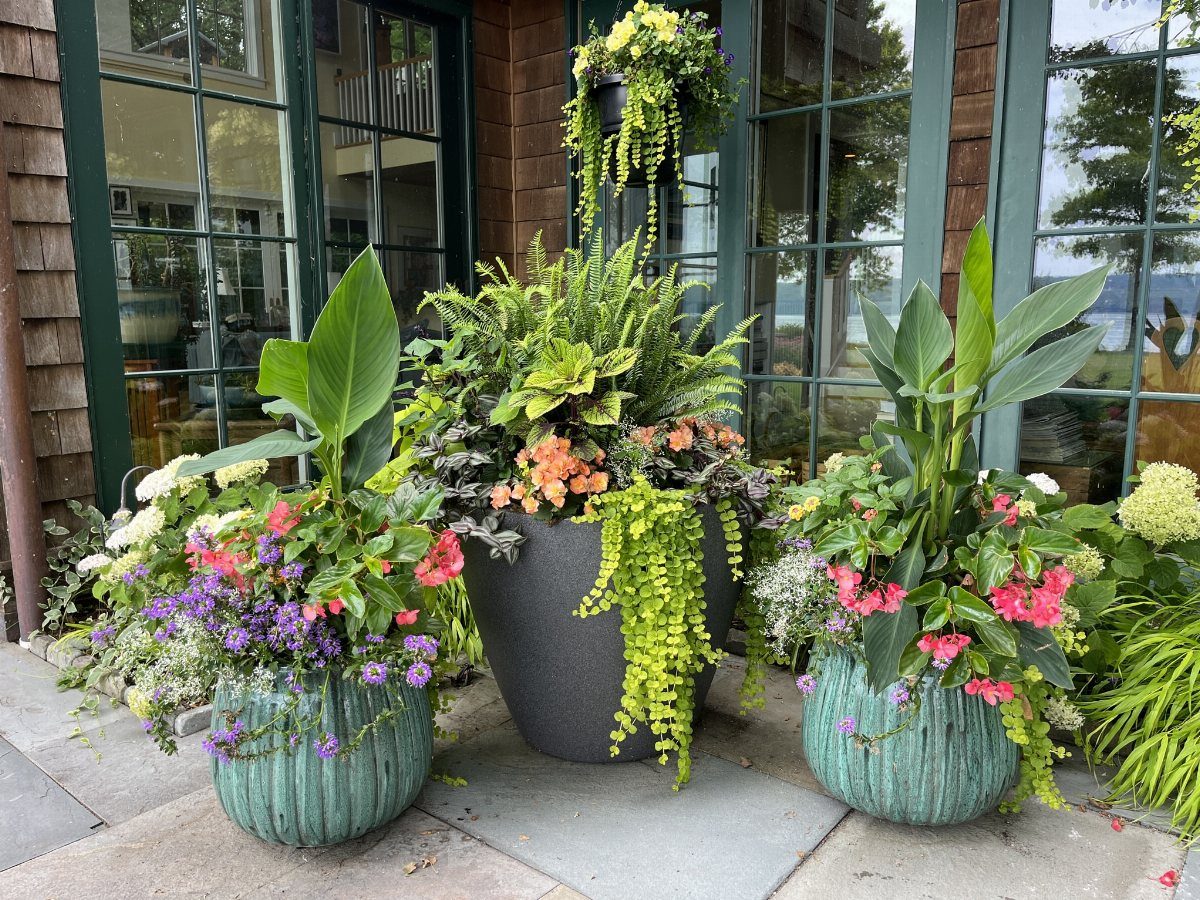 29 Outdoor Gardens Ideas for Patios, Yards, and Every Budget 14 Three large decorative planters filled with colorful flowers and lush greenery on a stone patio.