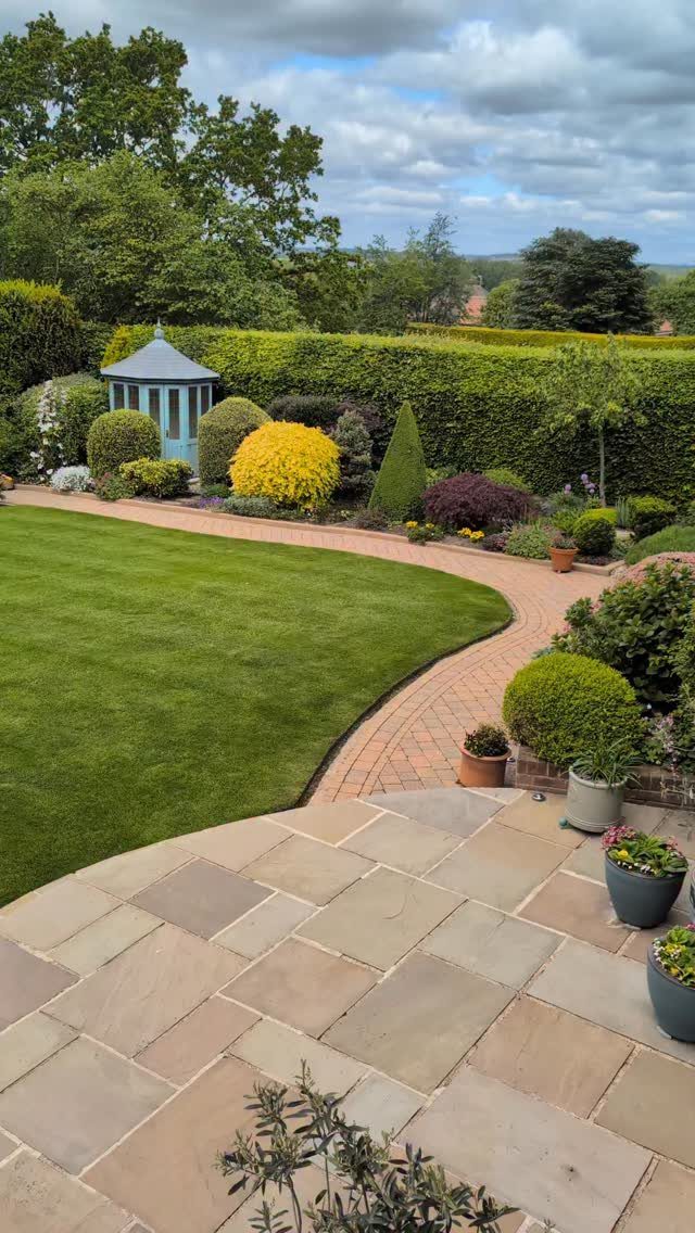 29 Outdoor Gardens Ideas for Patios, Yards, and Every Budget 11 Manicured garden with a curved brick path, green lawn, and various colorful shaped shrubs.