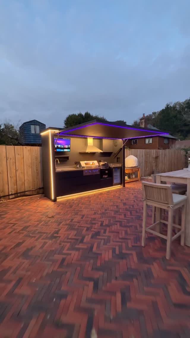 29 Outdoor Gardens Ideas for Patios, Yards, and Every Budget 27 Modern outdoor kitchen with built-in grill and purple LED lighting on a brick patio.