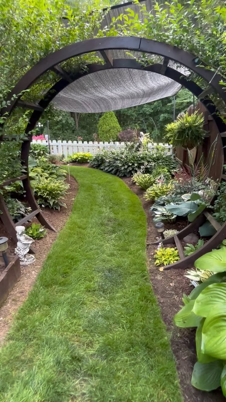 29 Outdoor Gardens Ideas for Patios, Yards, and Every Budget 6 A wooden arched pergola with a fabric shade covering a lush green garden path.