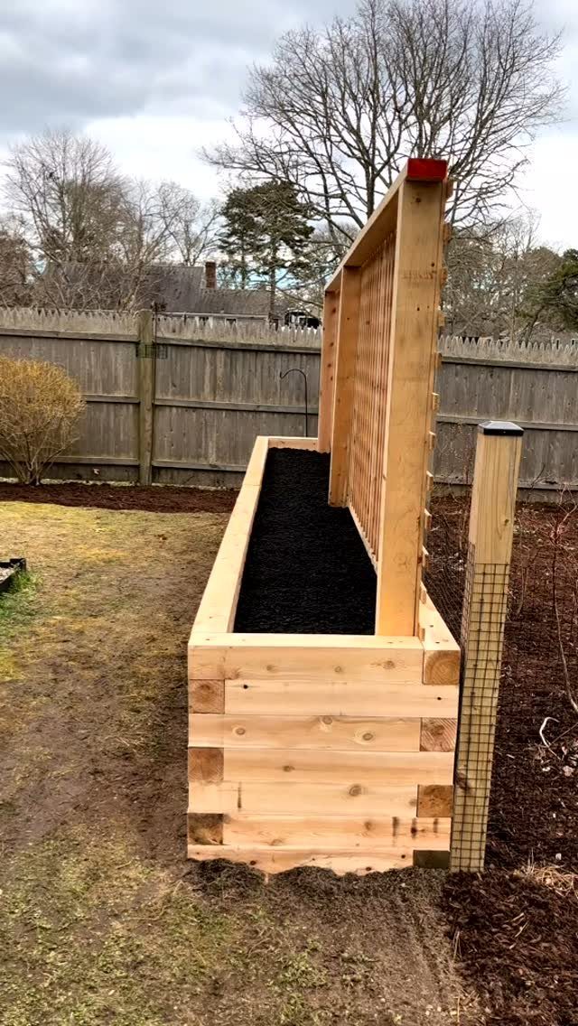Raised Garden Bed Ideas for Layout: 8 Photos to Plan From 7 A long wooden raised garden bed filled with dark soil standing in a backyard.