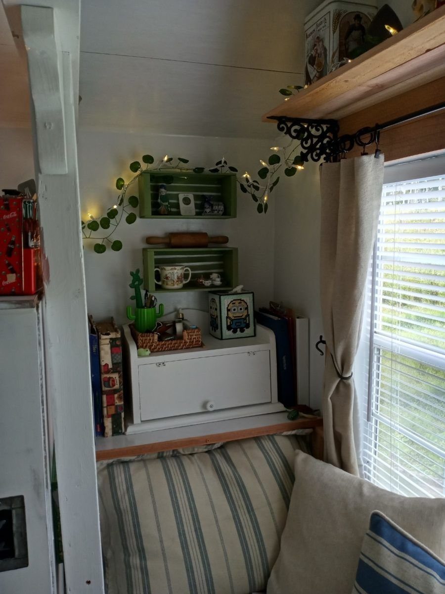 Small interior nook with white cabinetry, green shelves, string lights, and striped cushions near a window.