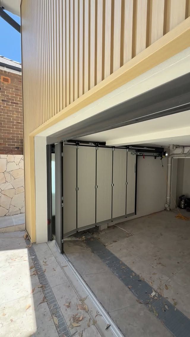 White folding garage door partially open, revealing a concrete garage interior and beige siding.
