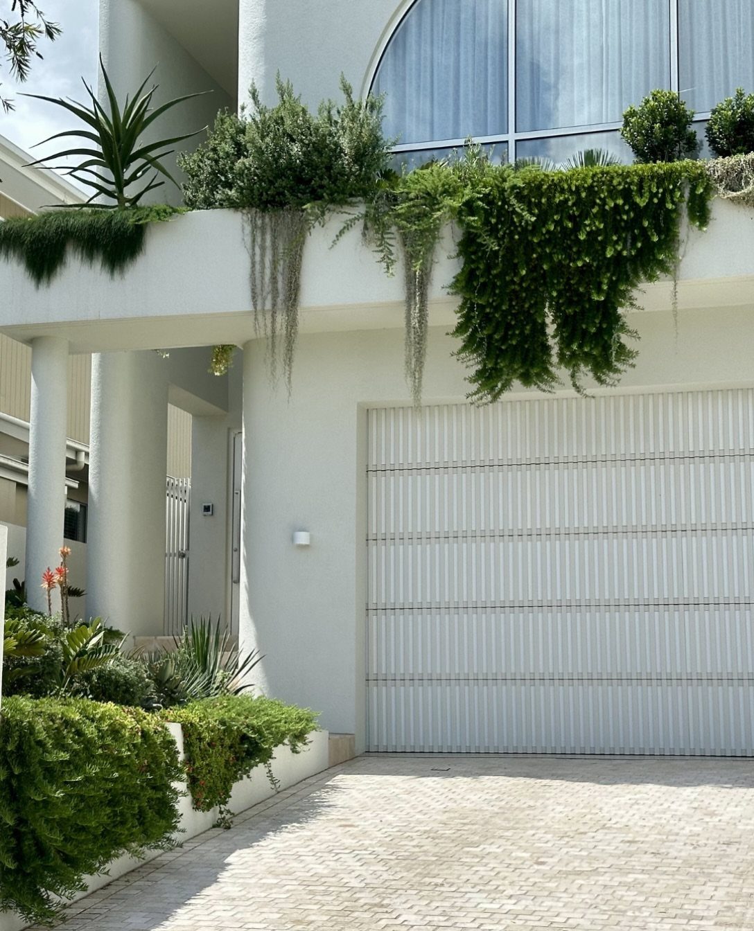 White garage door with lush green plants and hanging vines draping from the ledge above.