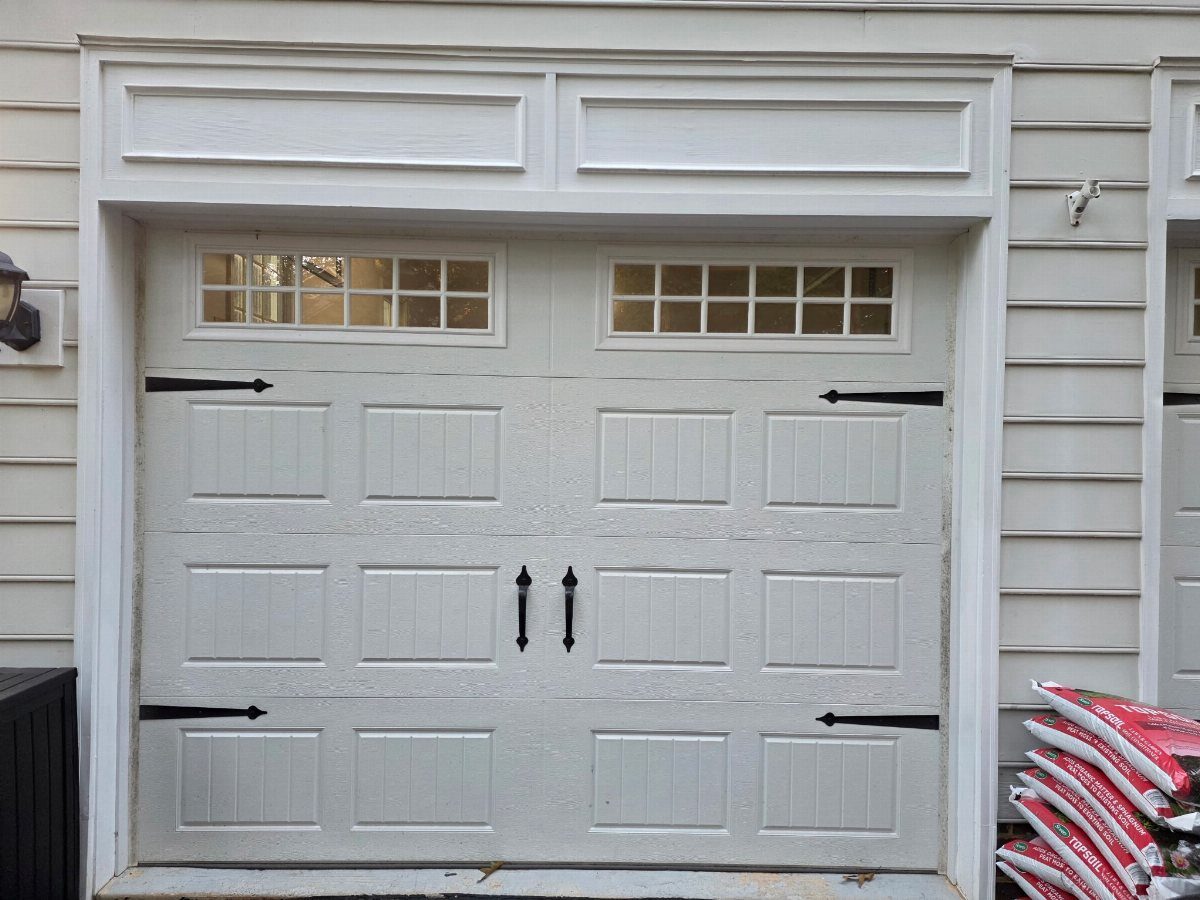 White garage door with black decorative hardware and small window panes on a white house.