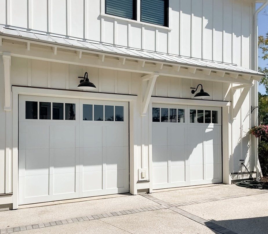 Two white garage doors with windows installed on a white board and batten exterior wall.
