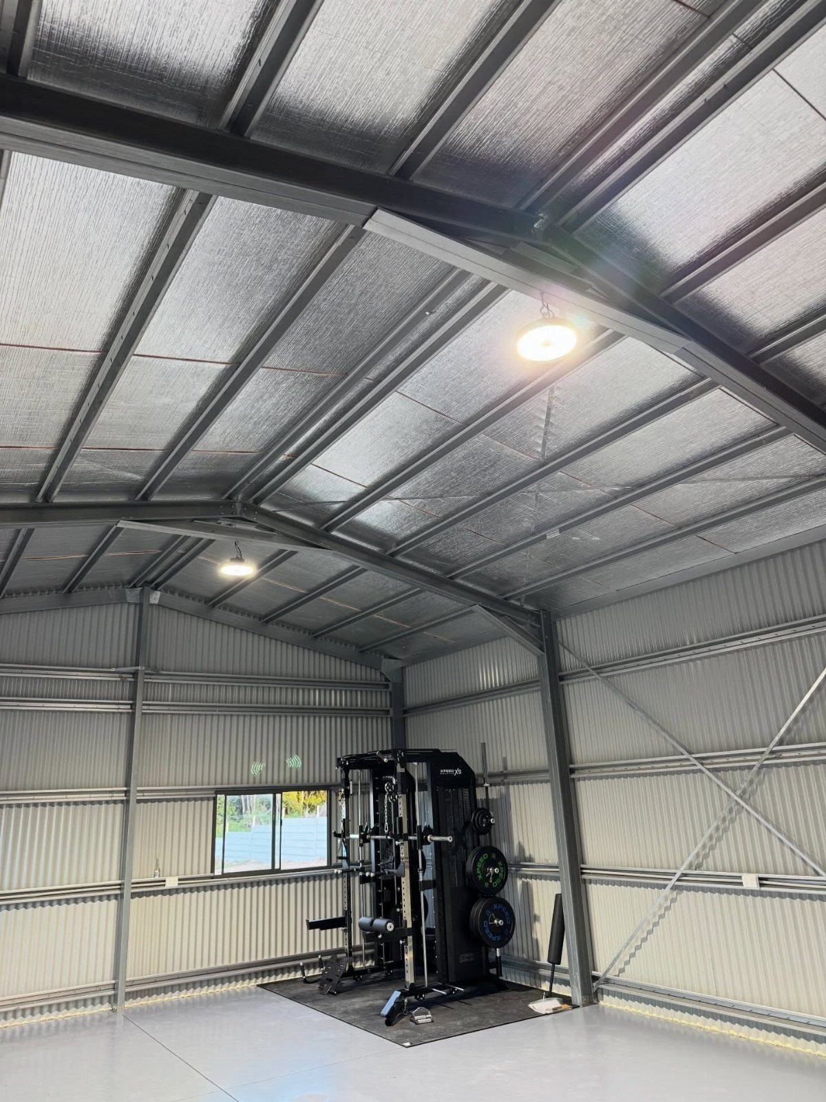 Metal shed gym interior featuring a black power rack and bright ceiling lights.